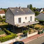 Maison surélevée sur pilotis avec terrasse surplombant le voisinage verdoyant et résidentiel