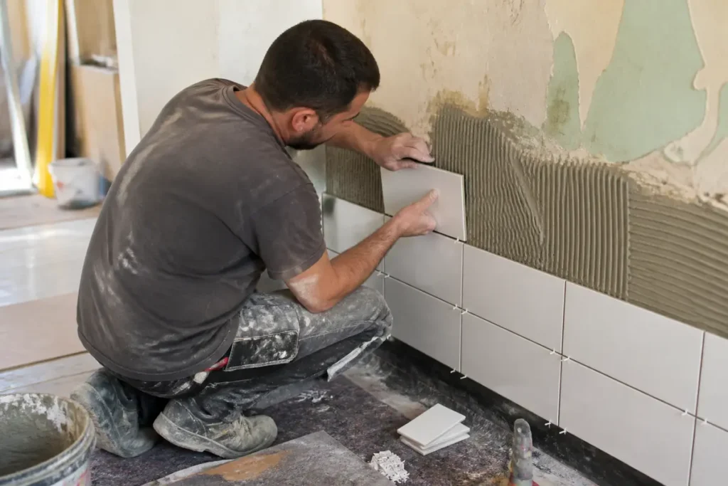 Carreleur posant des carreaux muraux dans une pièce en rénovation avec aquitainetravauxrenovation.fr.